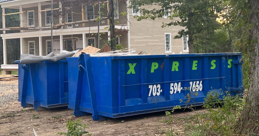 Two blue dumpsters are parked in front of a house under construction.