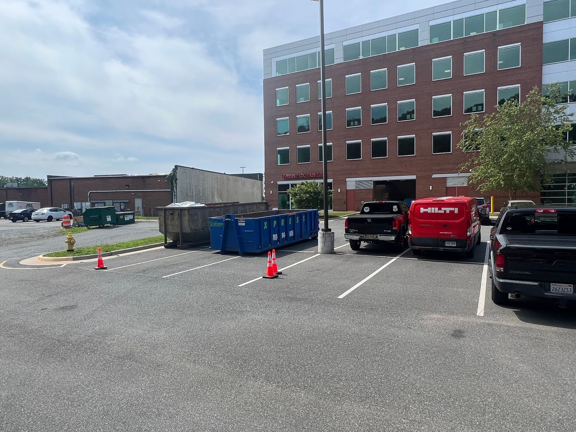 Parking lot with trucks, dumpsters, and a brick building under a cloudy sky.