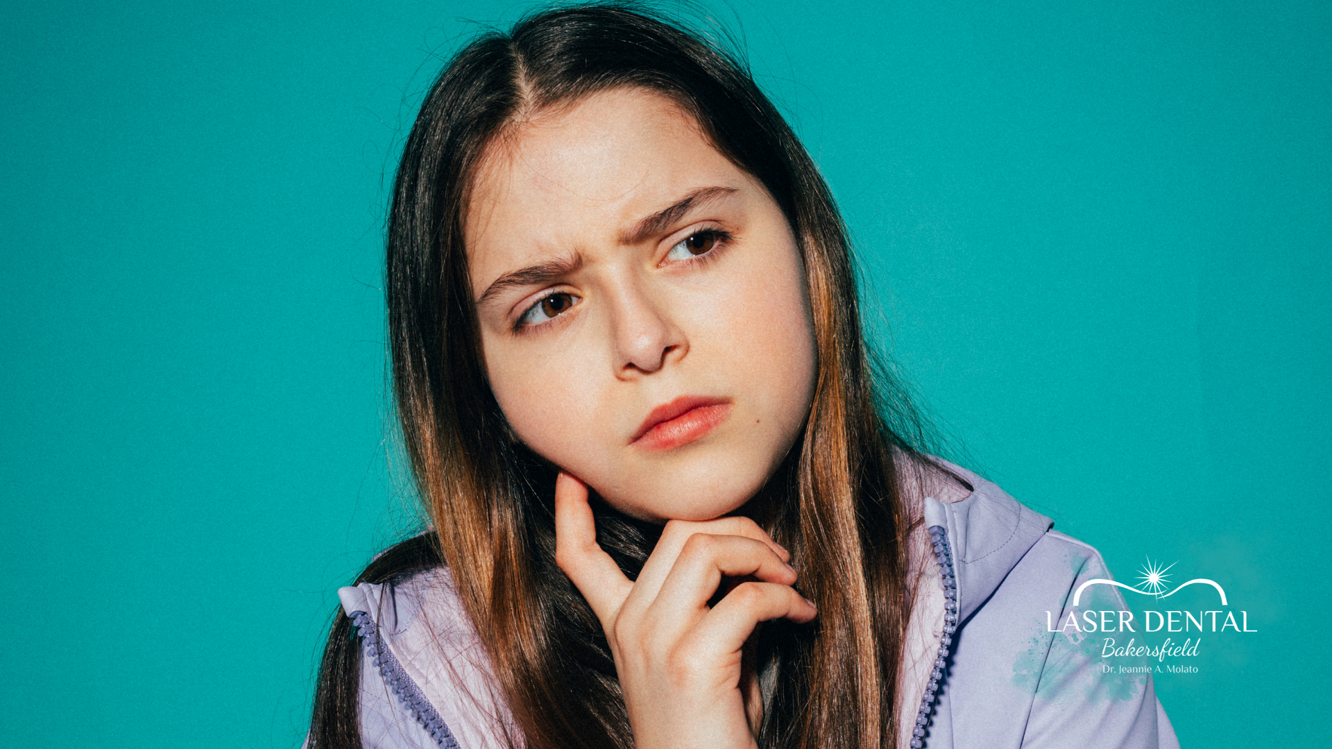 Girl with concerned expression, hand on chin, against turquoise background.