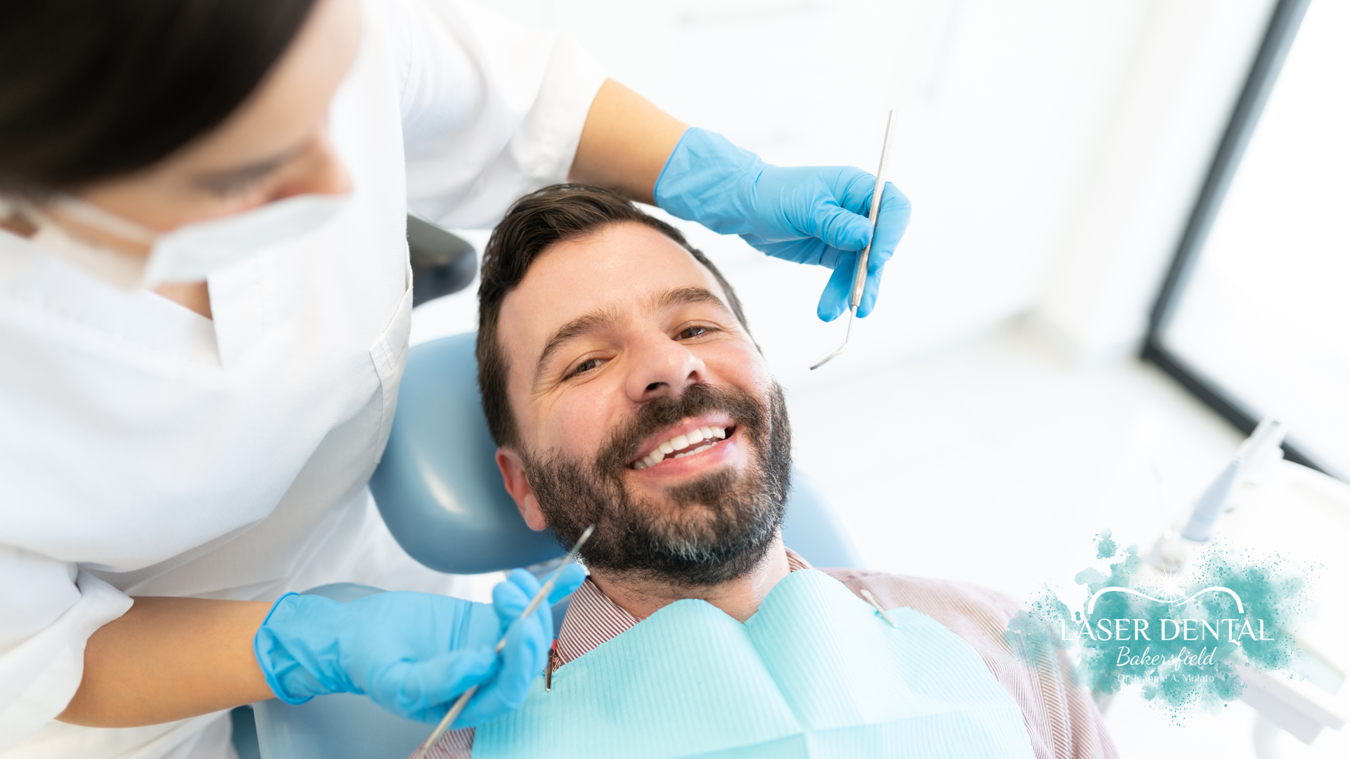 Man smiles during dental exam; dentist in gloves uses tools in a bright office.