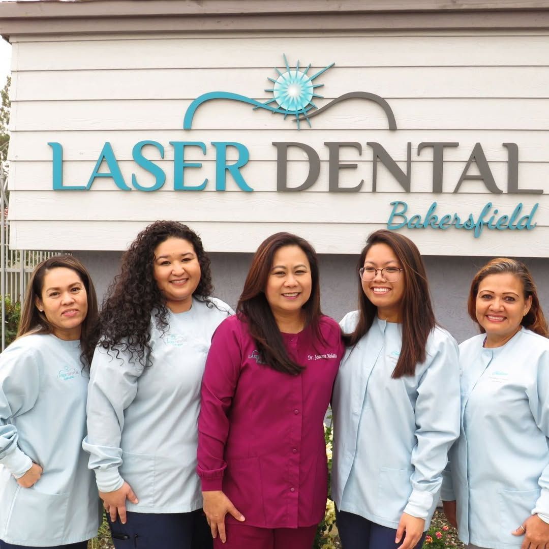Staff of Laser Dental Bakersfield smiling in front of the business sign; light blue scrubs, pink scrubs.