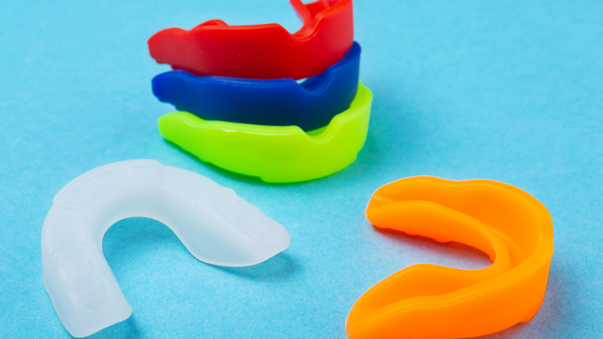 Stack of colorful mouthguards: red, blue, and green, with a white and orange mouthguard on a blue surface.