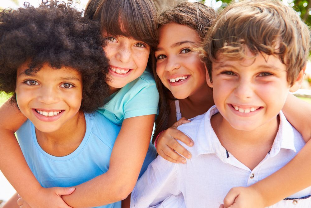 Four smiling children of diverse ethnicities hugging and looking at the camera.