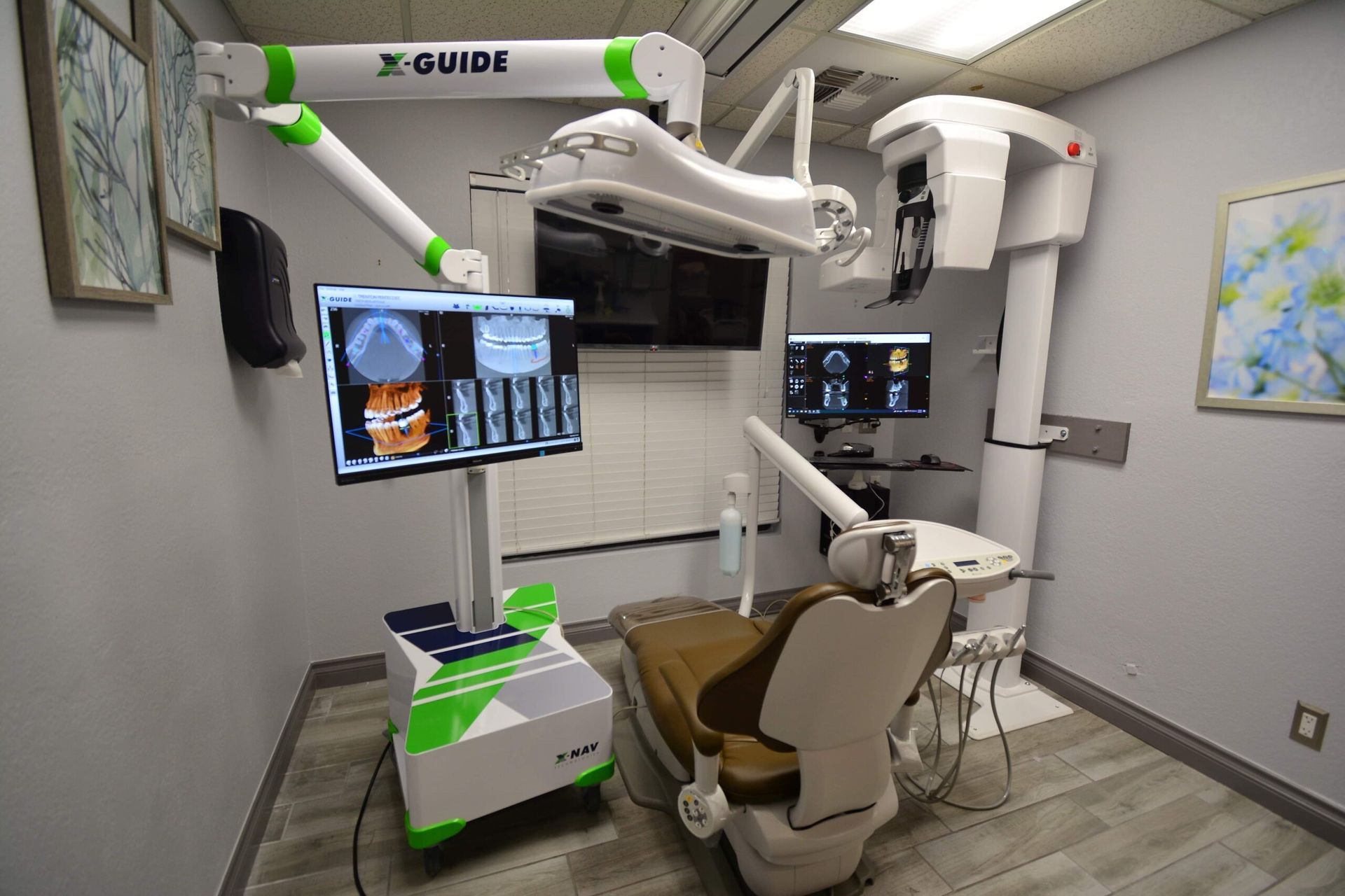 Dental office interior with X-Guide technology, chair, monitors displaying scans. Gray walls, green accents.
