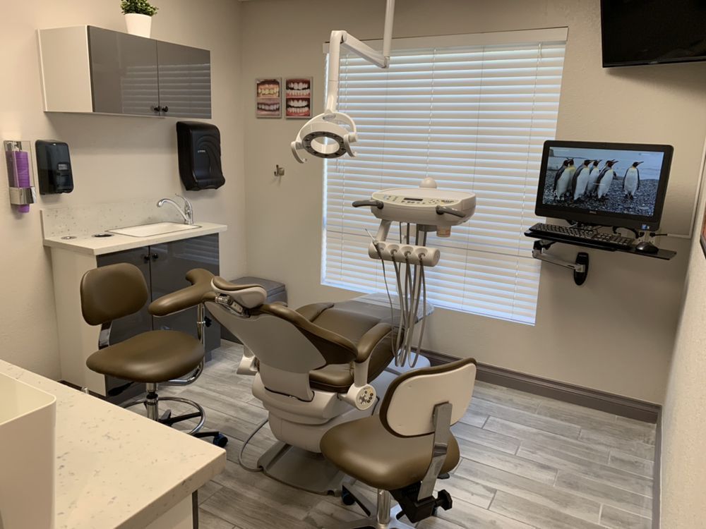 Dental office exam room with chair, tools, and computer; grey, brown, white color scheme.