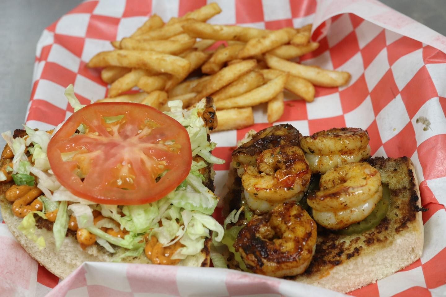 A sandwich with shrimp and french fries on a checkered paper.