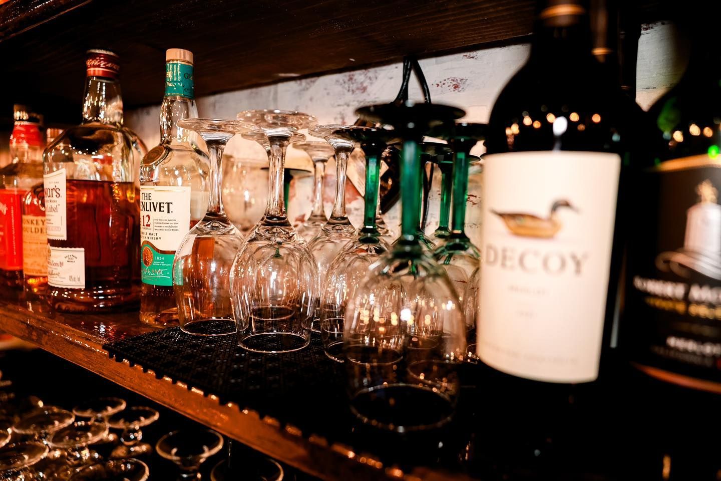 A bottle of decoy wine is sitting on a bar next to a row of wine glasses.