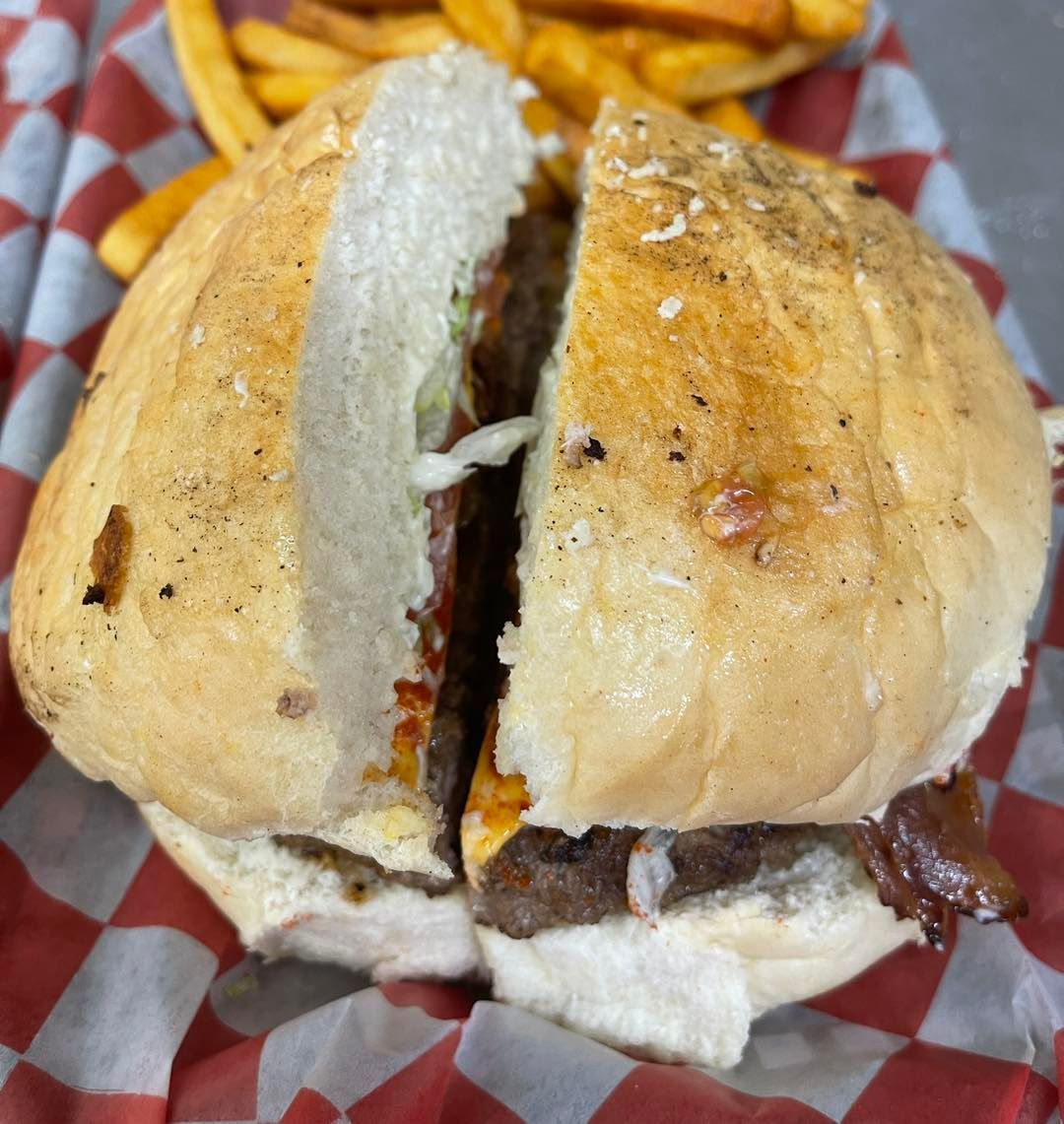 A hamburger is cut in half on a checkered napkin next to french fries