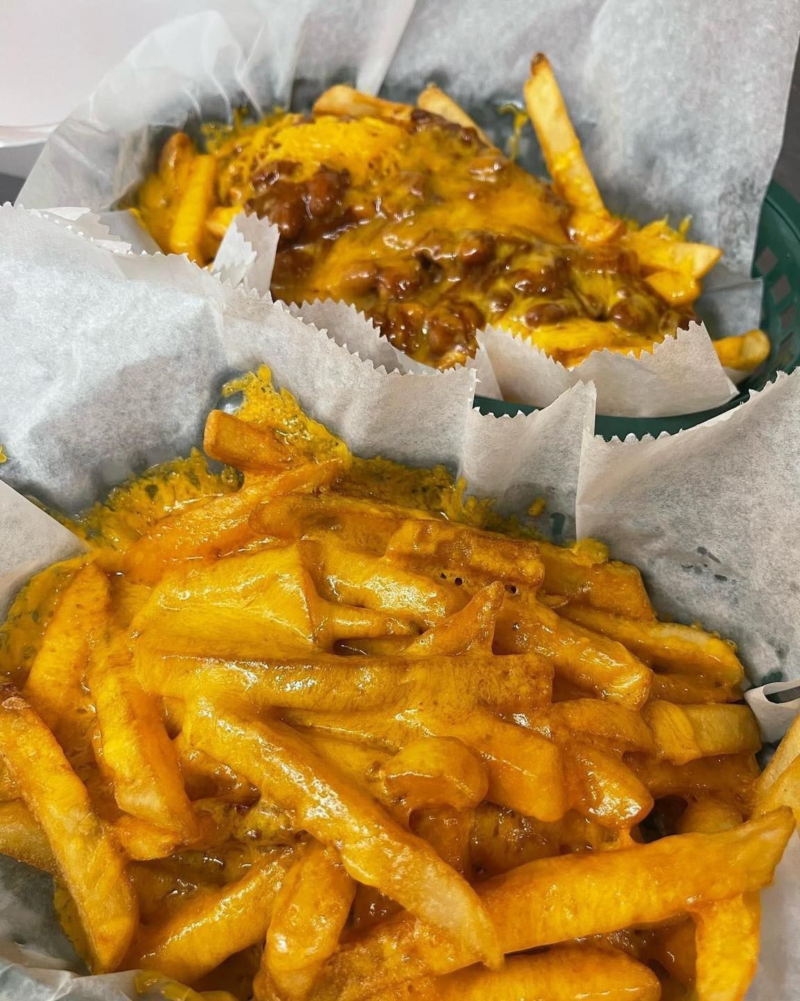 A close up of a basket of cheese fries on a table.
