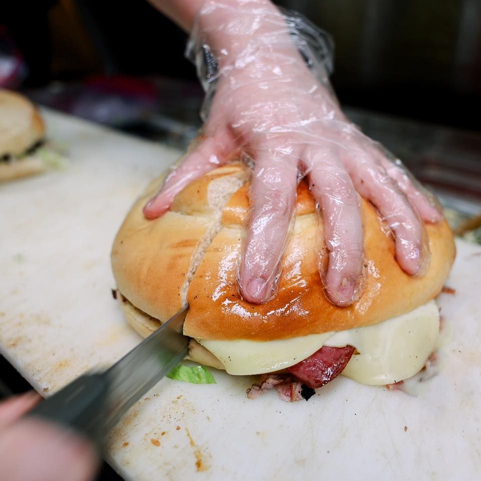 A person wearing plastic gloves is cutting a sandwich on a cutting board