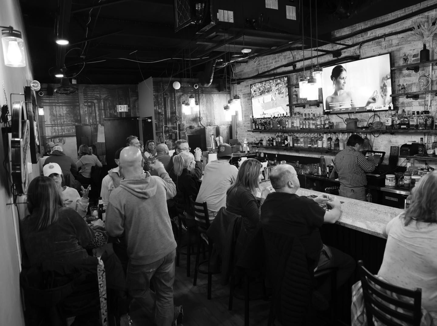 A black and white photo of people sitting at a bar in a restaurant.