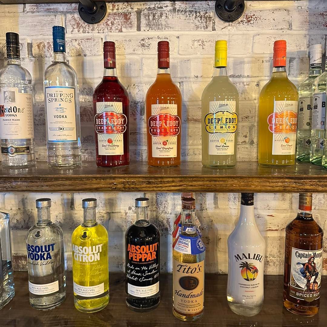 A variety of liquor bottles are lined up on a wooden shelf.