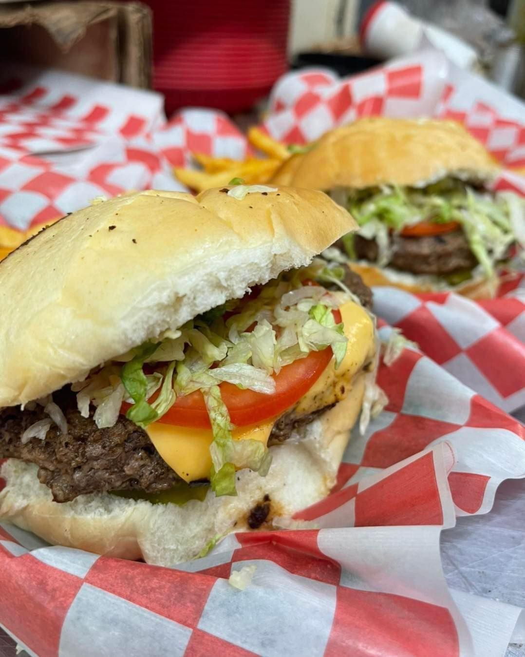 Two hamburgers are sitting on a checkered paper on a table.