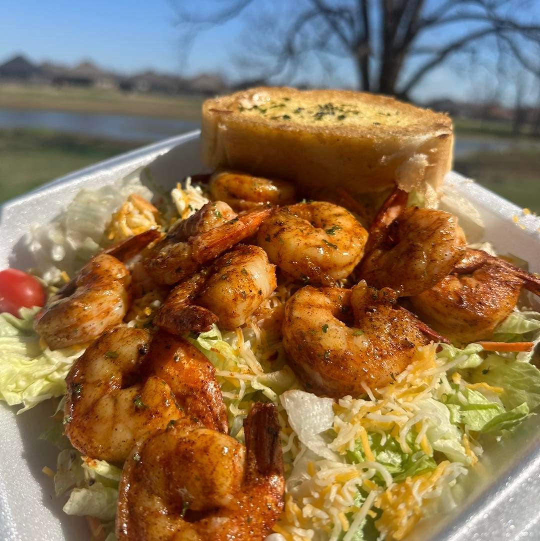 A styrofoam container filled with shrimp , lettuce , cheese and garlic bread.