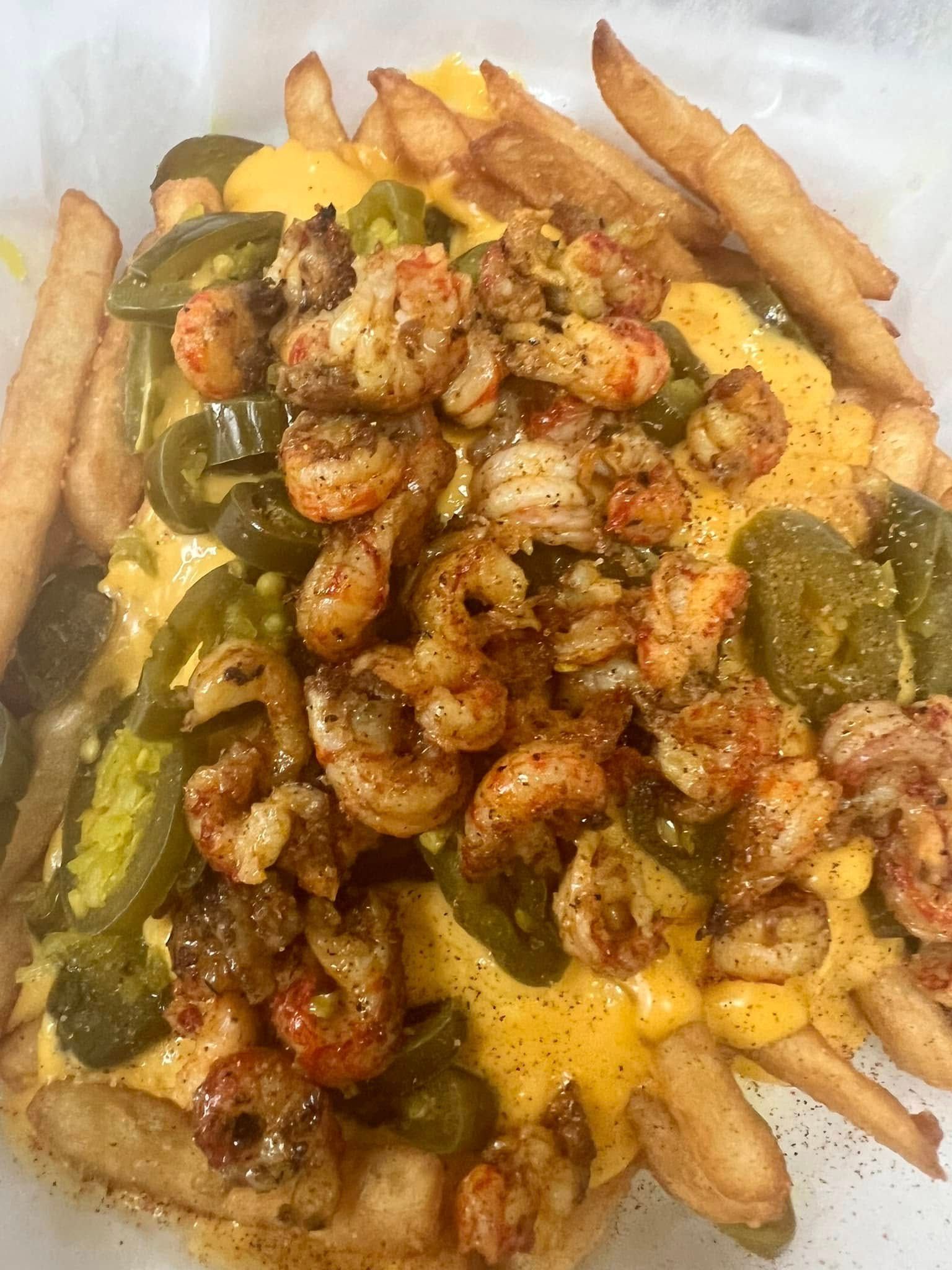 A close up of a plate of food with shrimp , cheese , jalapenos and french fries.