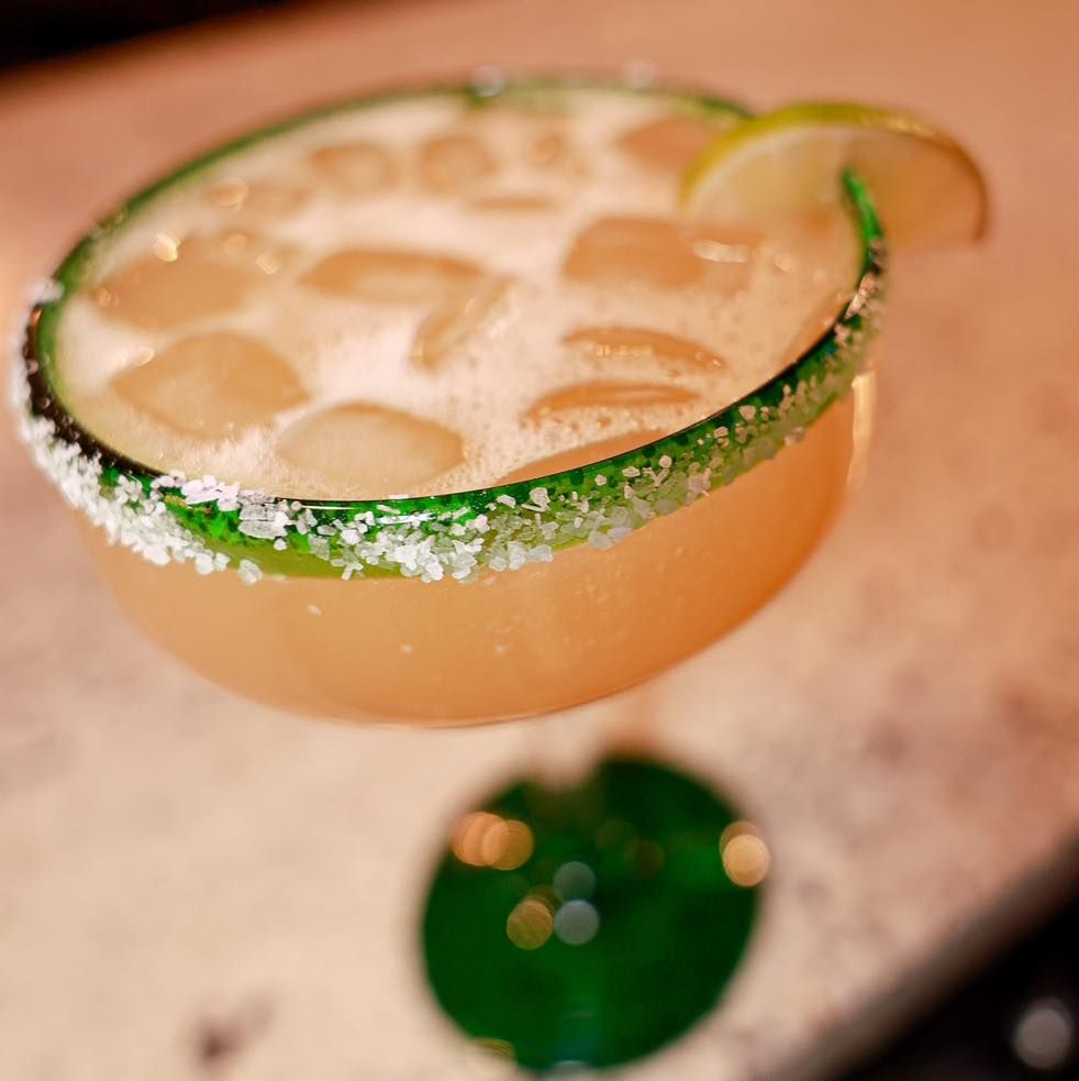 A close up of a margarita with a green rim on a table.