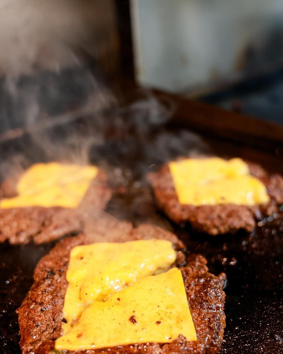 Three hamburgers with cheese on them are cooking on a grill.