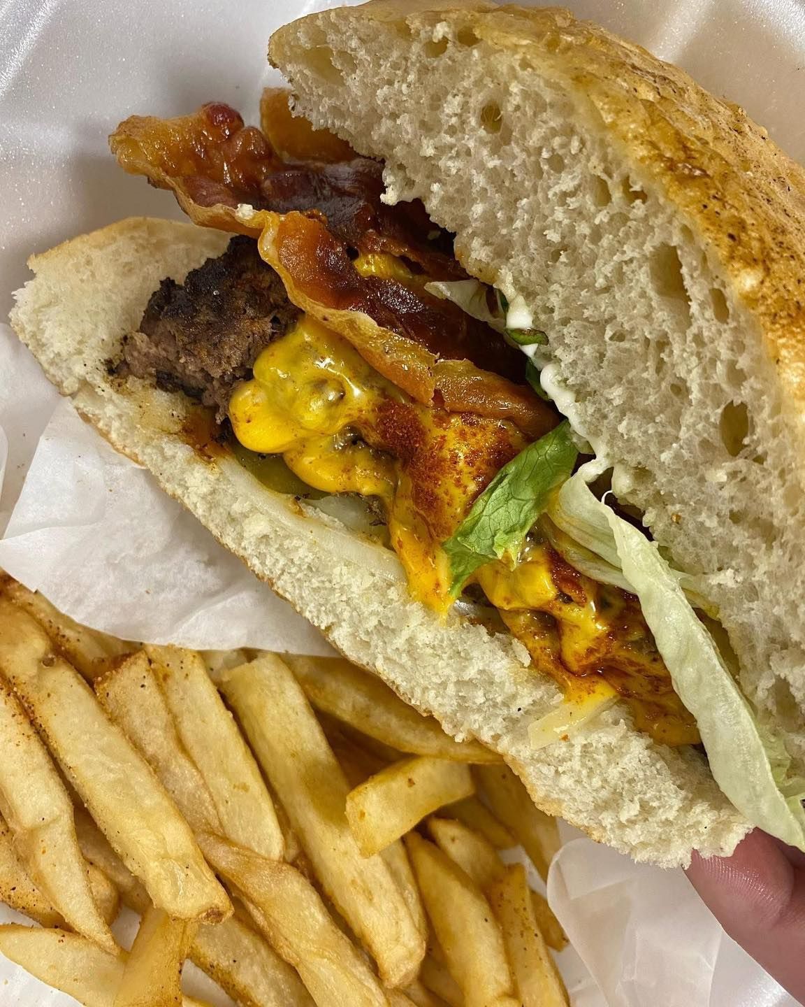 A person is holding a sandwich and french fries in a styrofoam container.