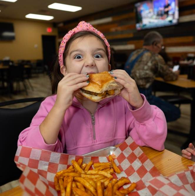 A little girl in a pink headband is eating a hamburger and french fries