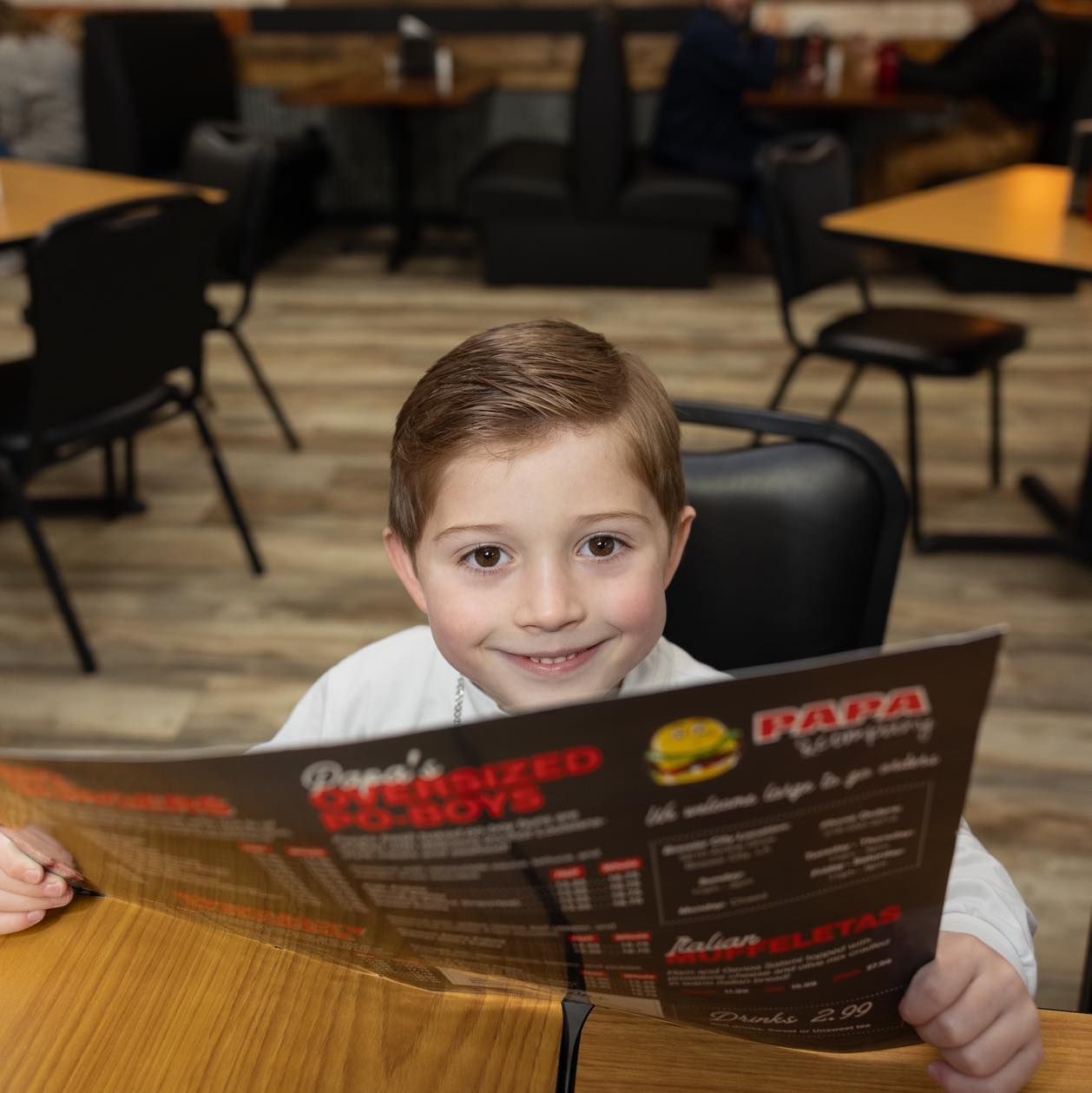 A young boy is reading a papa 's menu in a restaurant