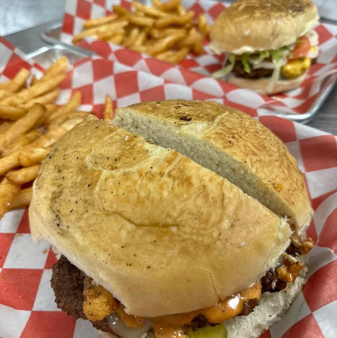 A hamburger is sitting on a checkered paper next to french fries