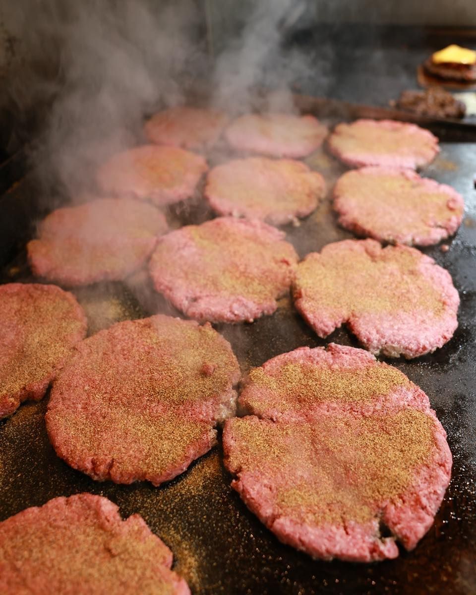 A bunch of hamburger patties are cooking on a grill.