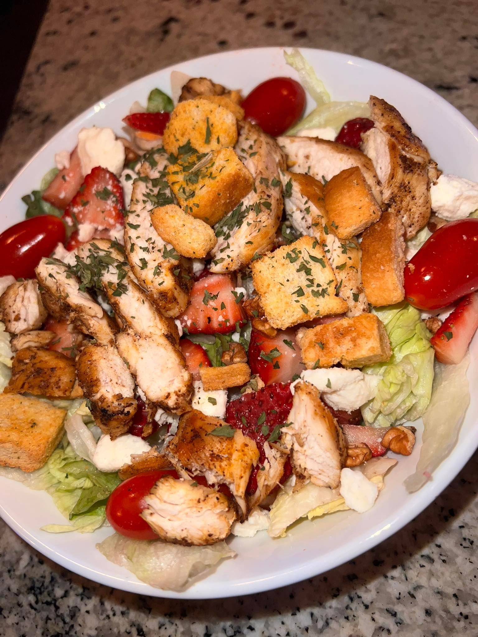 A white plate topped with a salad of chicken , lettuce , tomatoes and croutons.