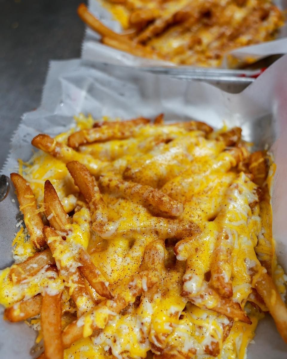 A close up of a plate of cheese fries on a table.