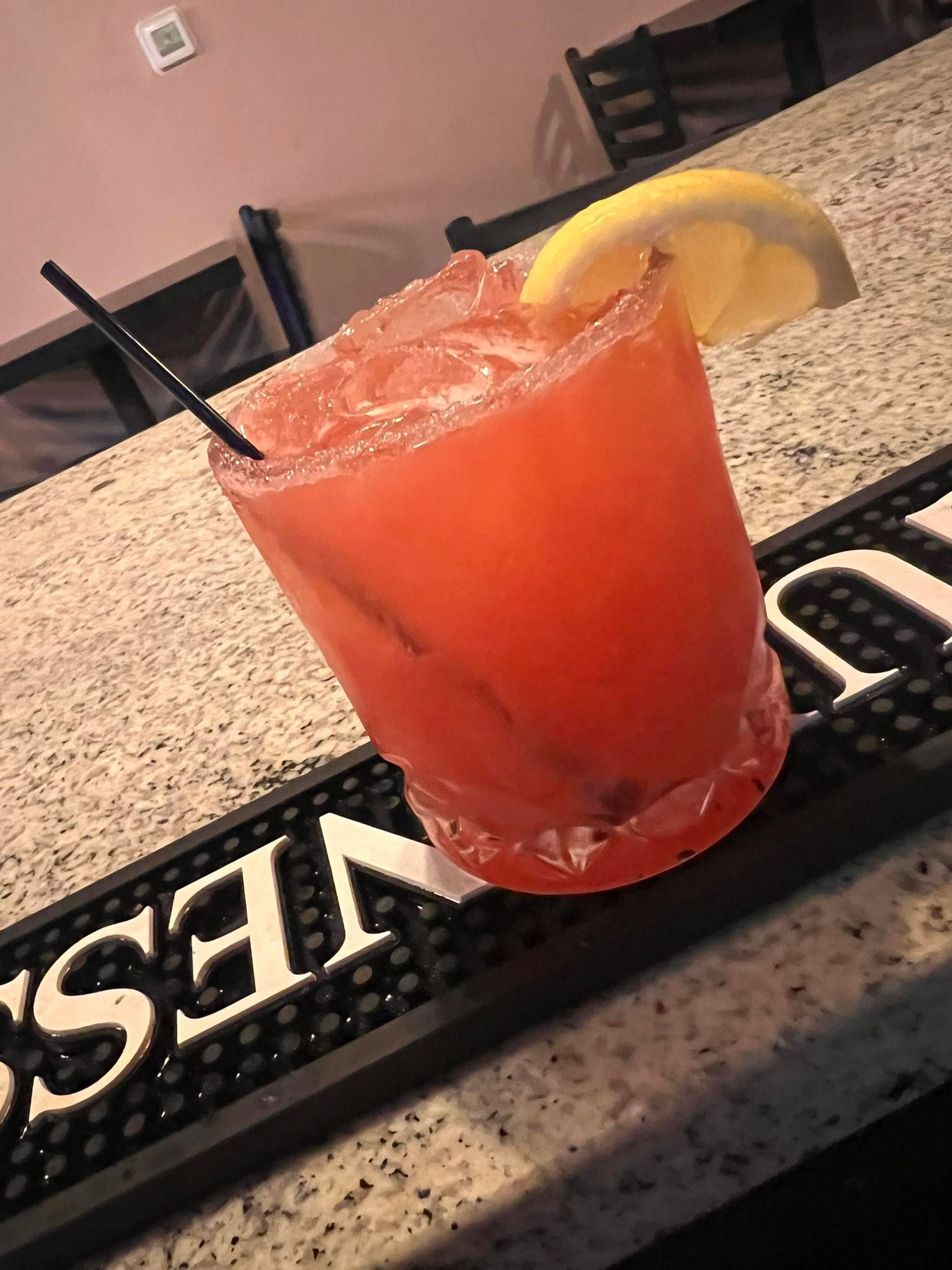 A red drink with a straw and a lemon slice is on a bar mat.