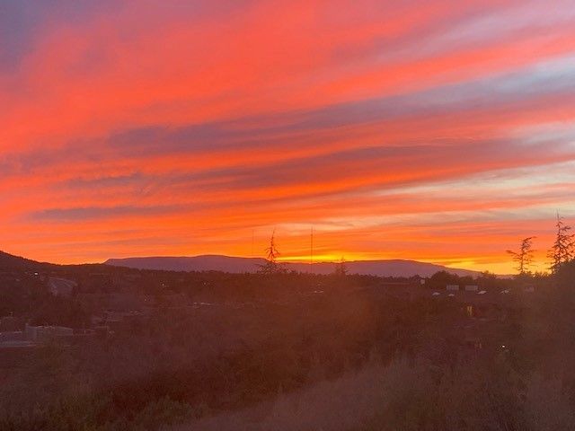 A colorful sunset over a mountain range with trees in the foreground.