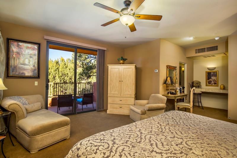 A hotel room with a king size bed , chairs , a desk and a ceiling fan.