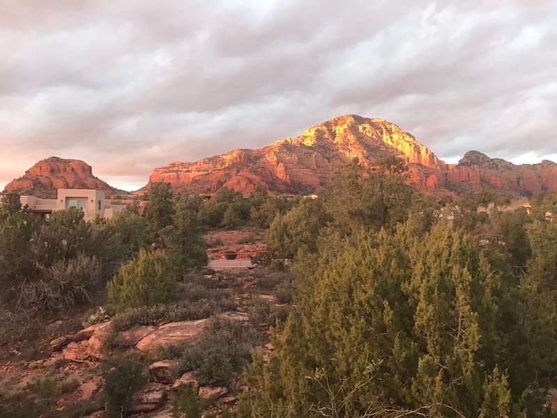 A mountain surrounded by trees and rocks with a cloudy sky in the background.