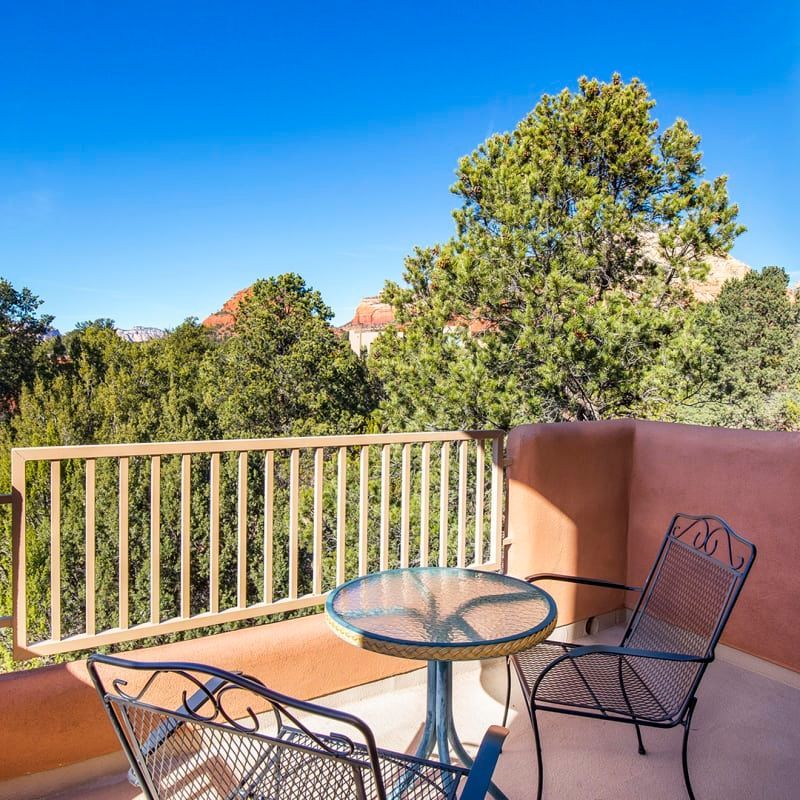 A balcony with a table and chairs with trees in the background