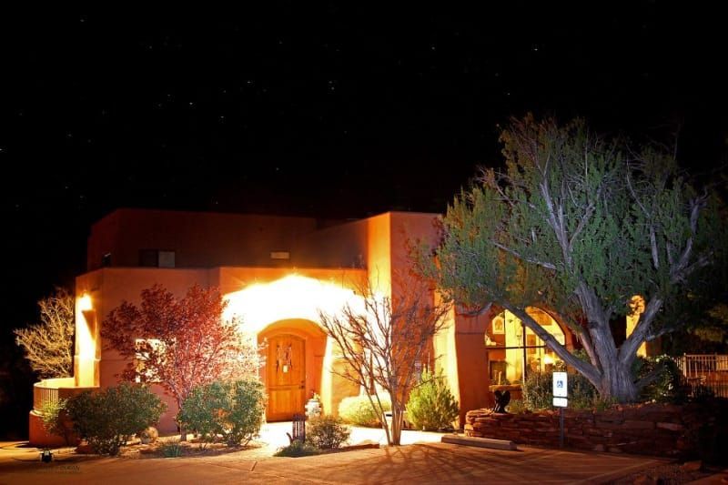 A house is lit up at night with trees in front of it.