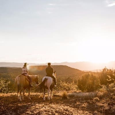 Two people are riding horses in a field at sunset.