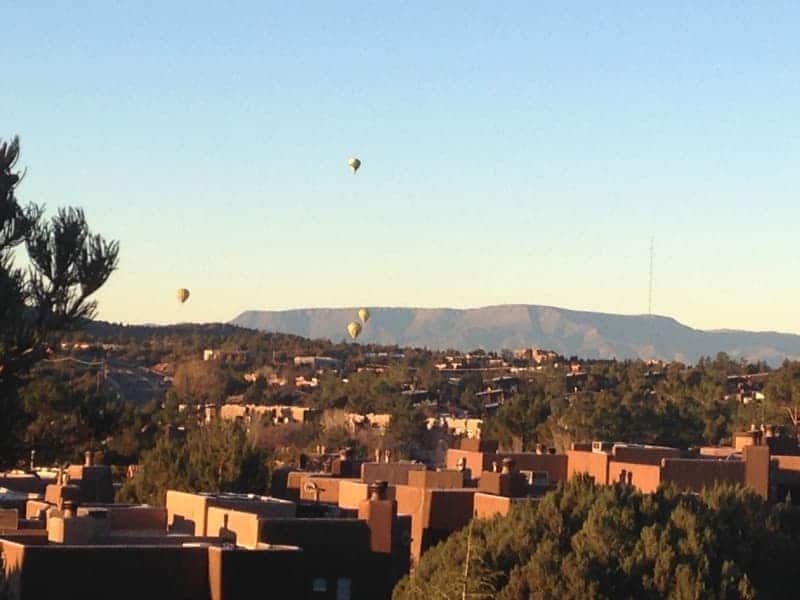 Hot air balloons are flying over a city with mountains in the background