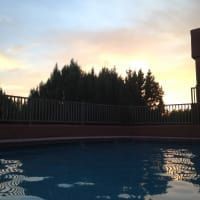 A swimming pool with a fence and trees in the background at sunset.