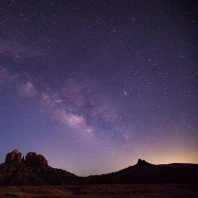 The milky way is visible in the night sky over a mountain range.