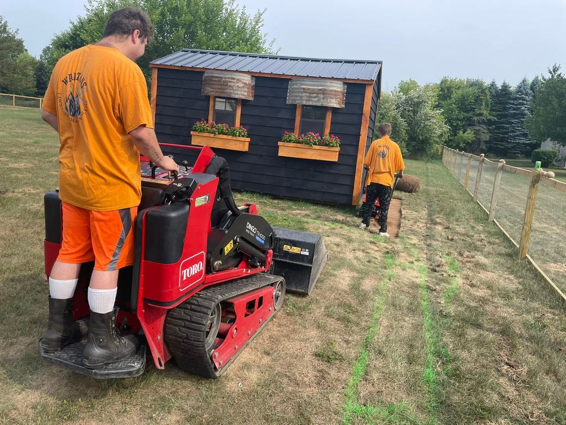 A man is riding a tractor in a field next to a shed.