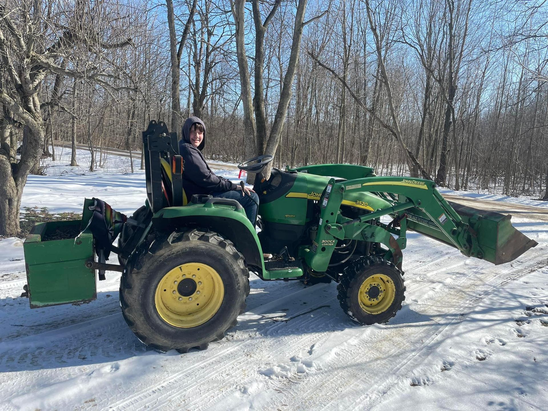 A man is driving a john deere tractor in the snow.