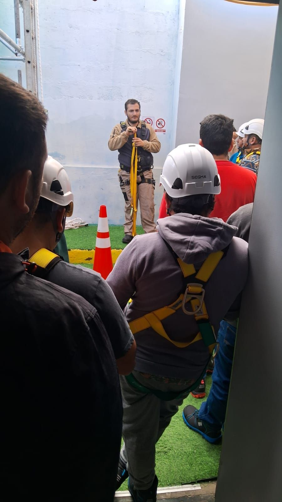 El instructor demuestra el equipo de seguridad a un grupo de personas que usan arneses en un entorno de capacitación.