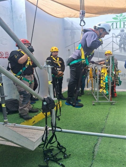 Persona con arnés de seguridad suspendida, preparándose para una aventura en tirolesa. Otros cerca le ayudan con el equipo.