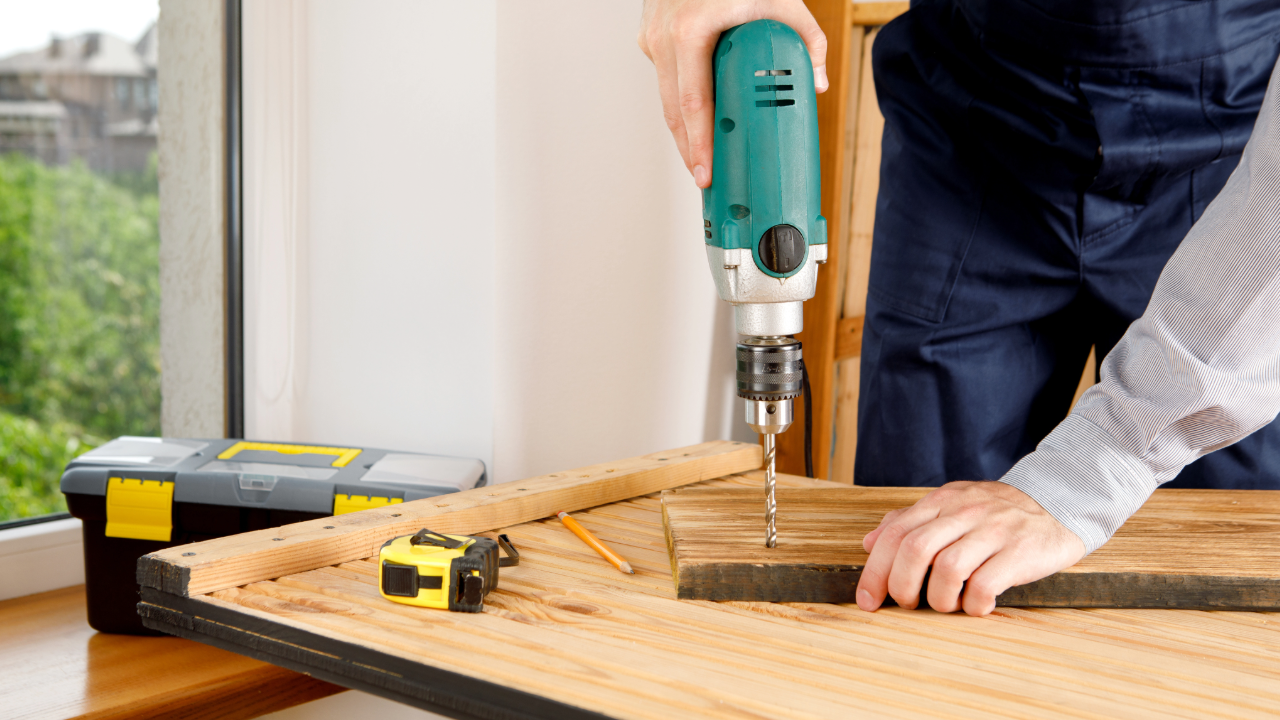 A man is using a drill to drill a hole in a piece of wood.