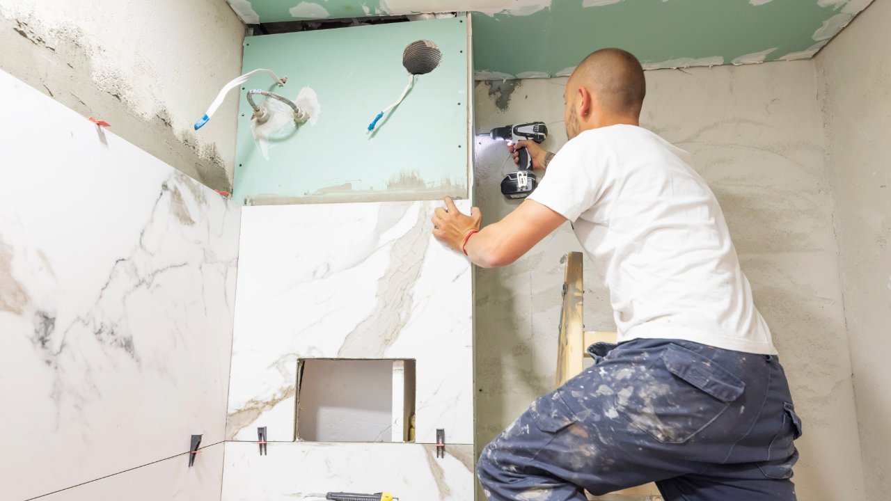 A man is using a drill to install a tile wall in a bathroom.