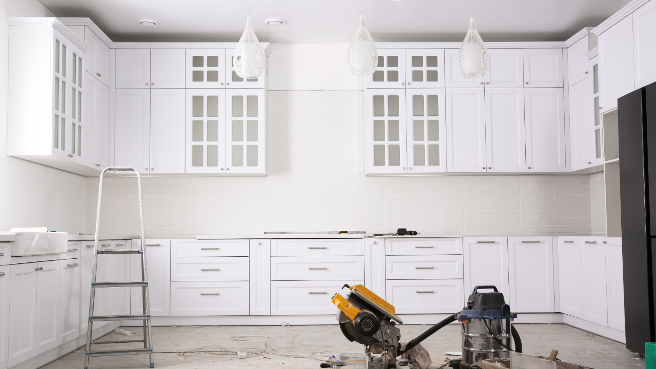 A kitchen under construction with white cabinets and a ladder.
