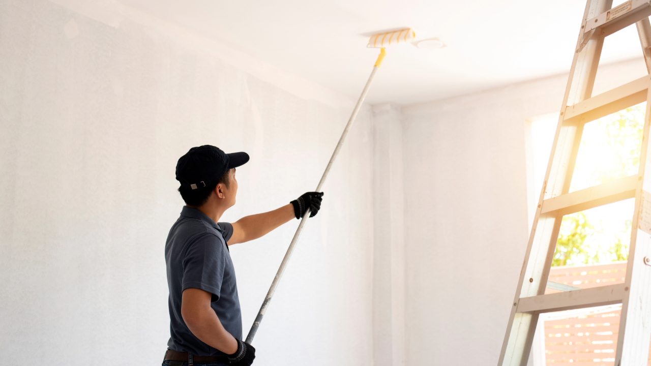 A man is painting the ceiling of a room with a paint roller.