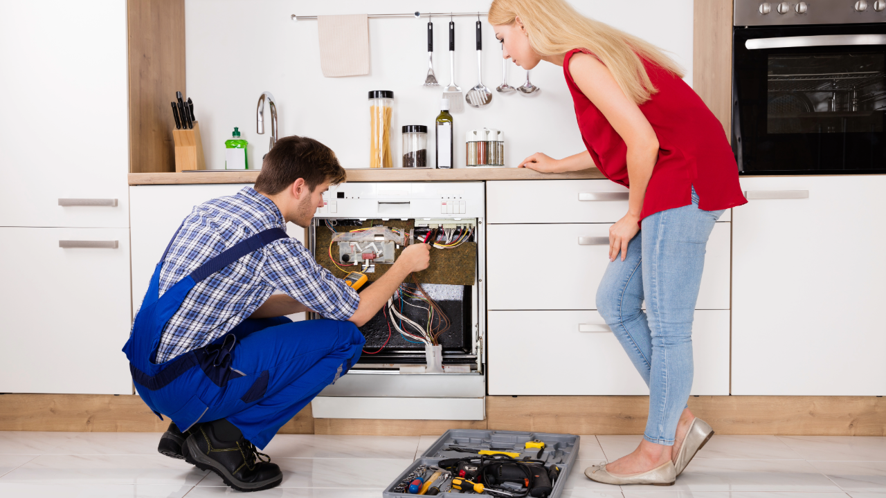 A man and a woman are working on a dishwasher in a kitchen.