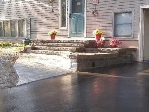 Home exterior with a paved driveway, front steps, and a blue door. Flower pots decorate the steps.