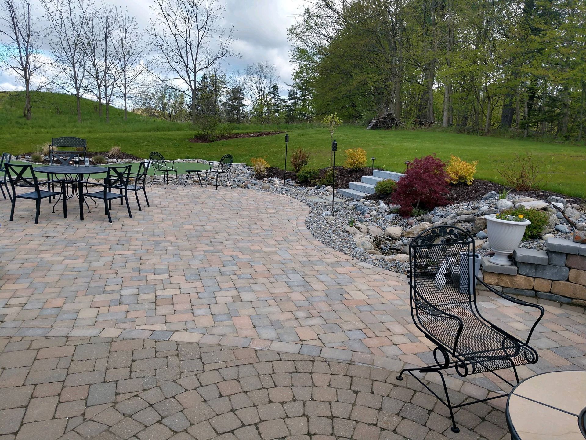 A patio with tables and chairs and a lush green field in the background.