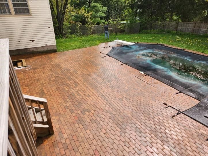 A man is standing on a brick patio next to a swimming pool.